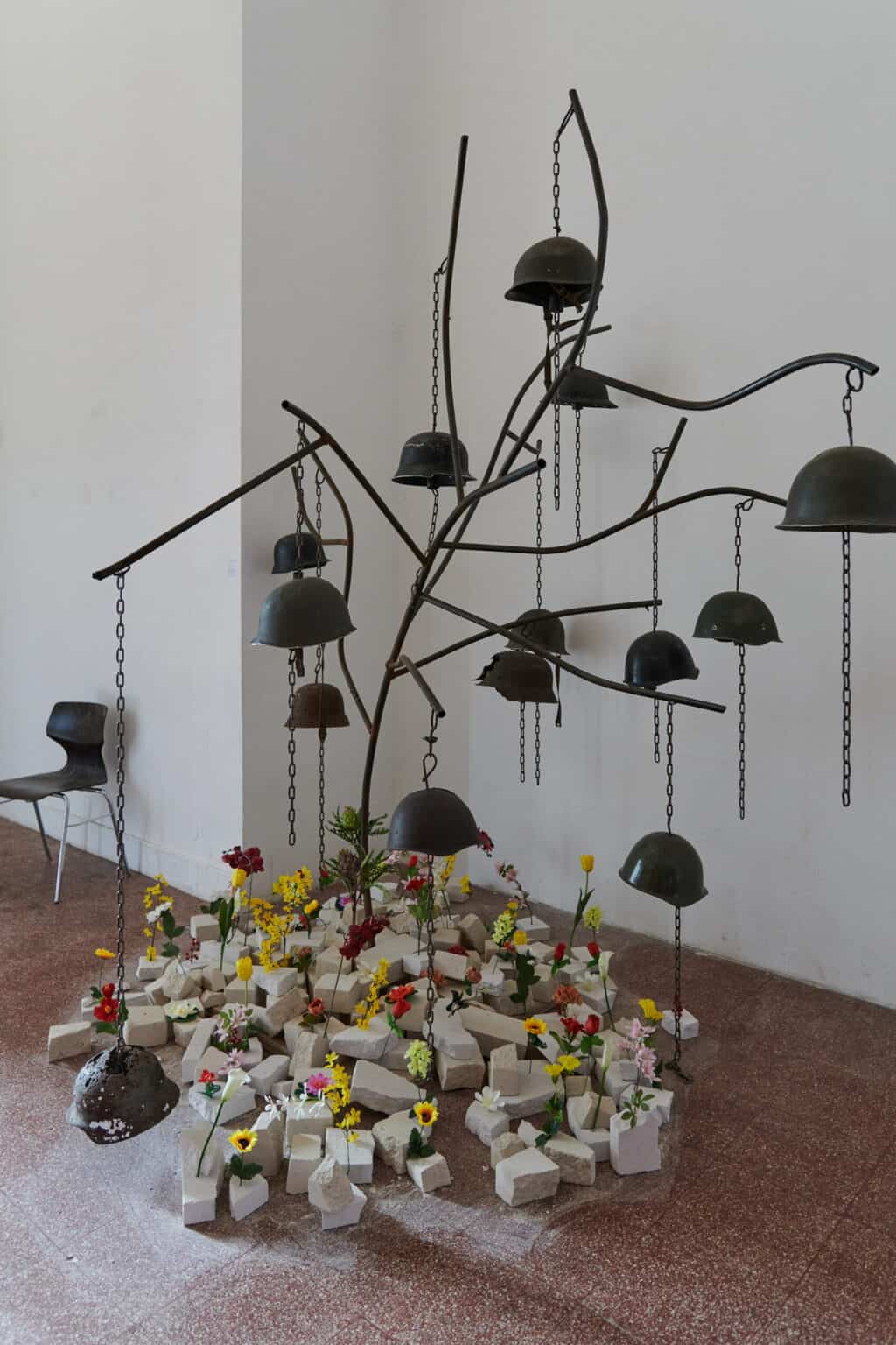 Foto: Ansicht eines Raumes mit weißen Wänden und rotem, gefliesten Steinboden. Im Raum befindet sich eine Gruppe von Objekten, die ineinander gesteckt sind.