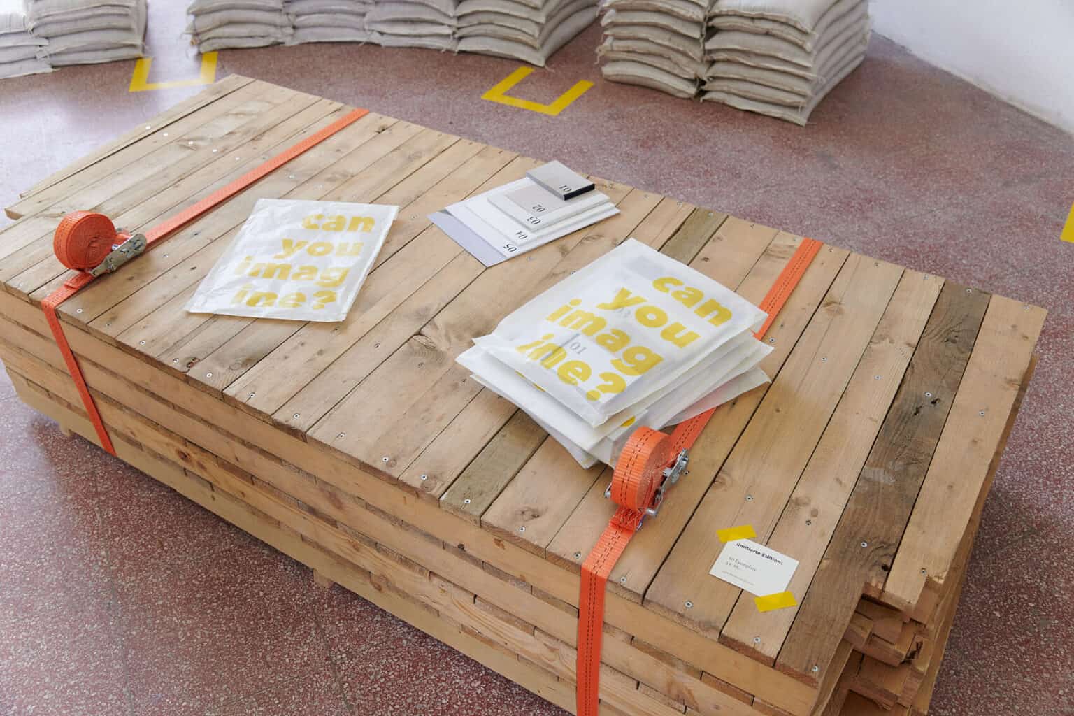 Foto: Detailaufnahme zusammengeschnürter Paletten, auf denen Objekte liegen, vor rotem Steinboden.