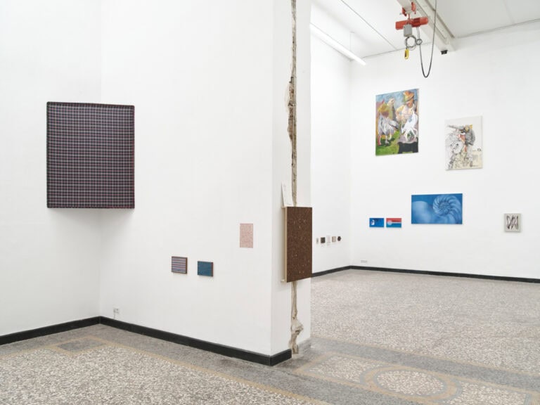 Foto: Ansicht eines Raumes mit weißen Wänden, schwarzer Fußleiste, und mehrfarbigen Steinboden. An den Wänden des Raumes befinden sich Objekte und Malereien in Klein-, Mittel- und Großformaten.