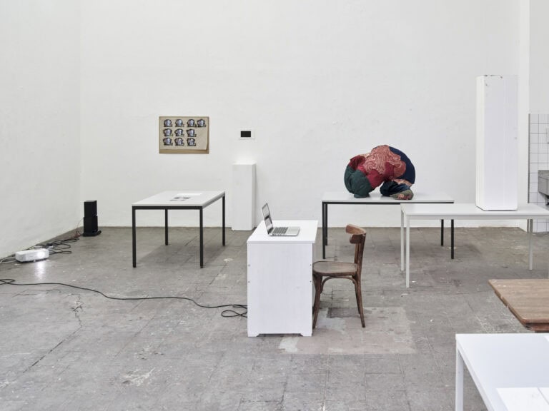 Foto: Ansicht eines Raumes mit weißen Wänden und grauem, gekachelten Boden. Im Raum befinden sich Möbel, darunter Tische und Stühle, und weitere Objekte. Manche der Objekte hängen an der Wand, andere liegen oder stehen auf Tischen.