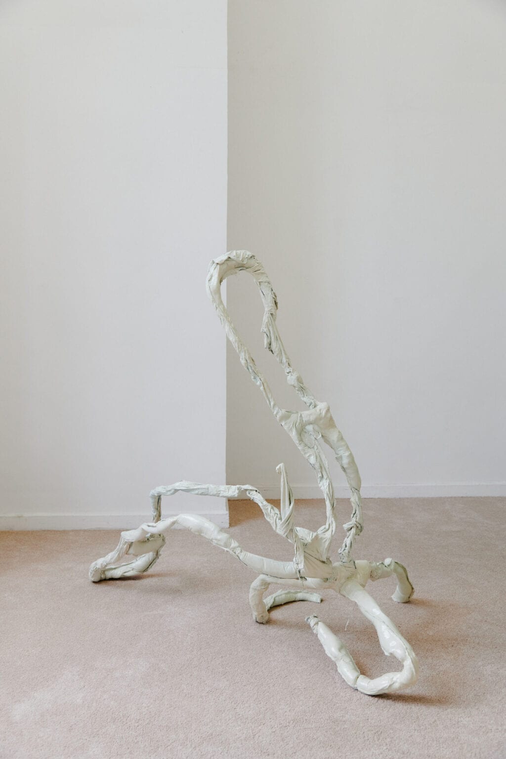 Foto: Ein Raum mit weißen Wänden und beigem Teppichboden. Im Raum eine große, gewundene Skulptur in Pastellfarbe.