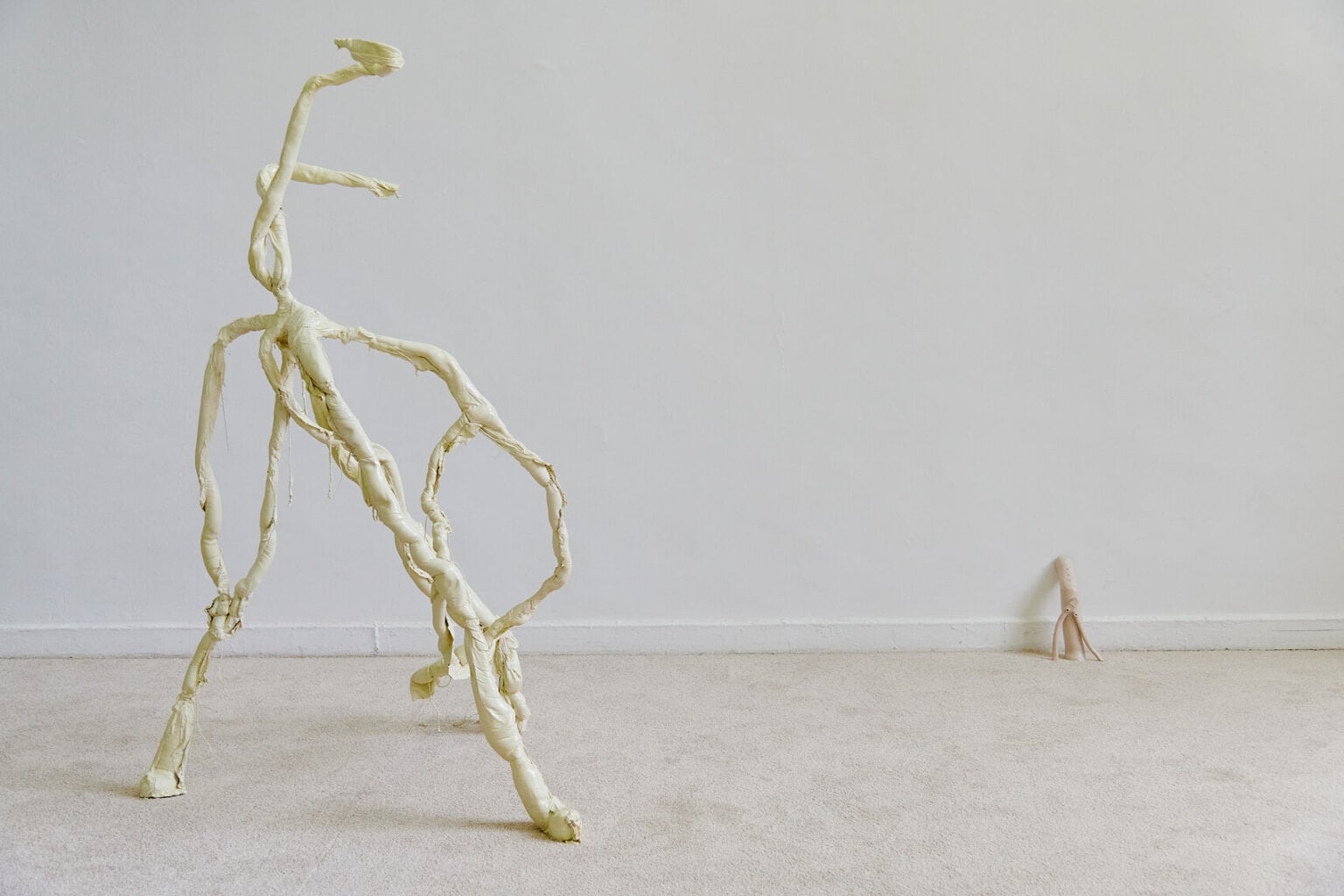 Foto: Ein Raum mit weißen Wänden und beigem Teppichboden. Im Raum verteilt zwei Skulpturen in Pastellfarben in unterschiedlichen Größen.