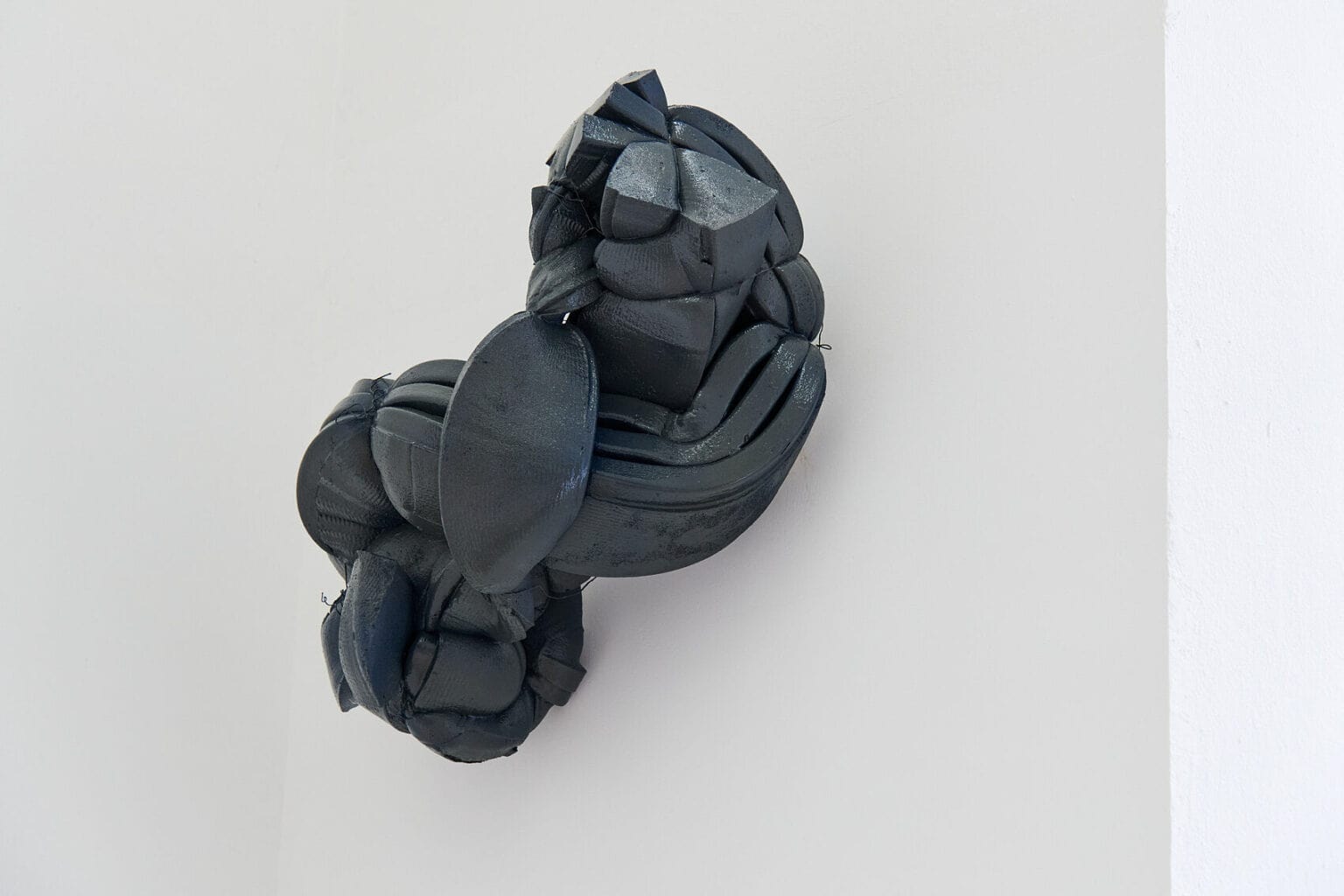 Foto: Ein geschnürtes, schwarzes Objekt vor weißer Wand.