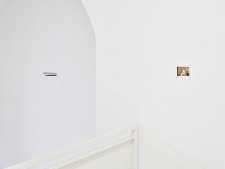 Foto: Ansicht eines Raumes mit weißen Wänden. An der Wand hängt ein mit Nägeln fixiertes, flaches Objekt.