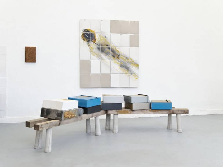 Foto: Ansicht eines Raumes mit weißen Wänden und grauem Boden. An den Wänden und im Raum befinden sich Objekte.