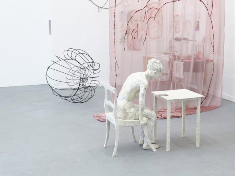 Foto: Ansicht eines Raumes mit weißen Wänden und grauem Boden. Im Raum befinden sich eine Vielzahl von Objekten, Textilien und Malereien.