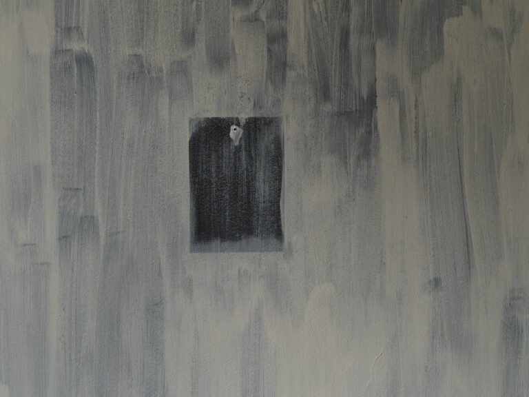 Foto: Nahaufnahme einer fleckig gestrichenen, cremefarbenen und blauen Wand. In der Wand befindet sich ein kleines Loch und eine Quadratische Aussparung, auf dem allein der bläuliche Ton der Wand zu sehen ist.