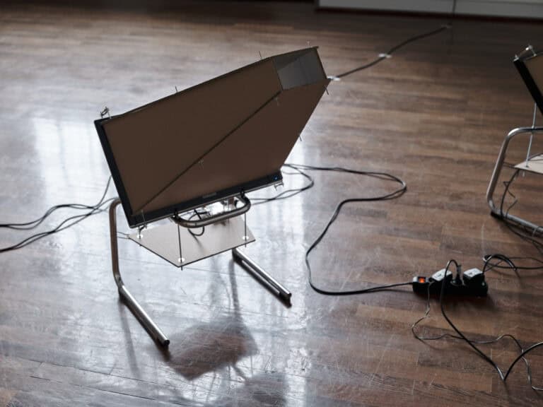 Foto: Ein Objekt und damit verbundene Kabel vor braunem Dielenboden mit spiegelnder Oberfläche