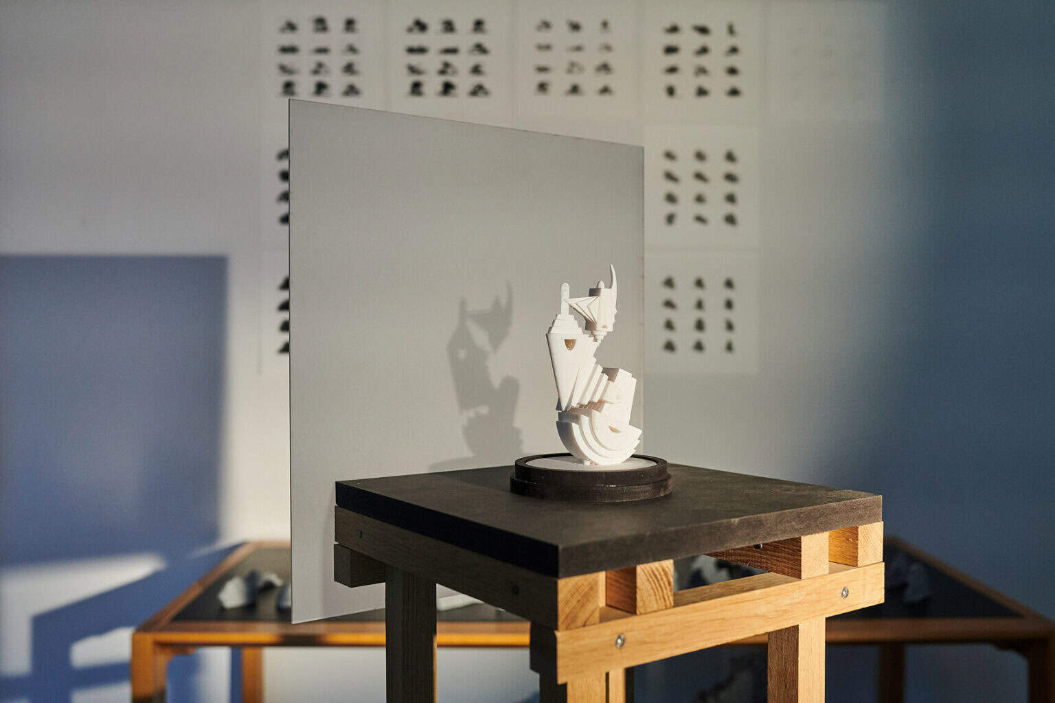 Foto: Detailaufnahme eines Objektes aus unterschiedlichen Materialien, dass von Licht angestrahlt wird. Ein Schatten fällt auf eine in das Objekt integrierte Platte.