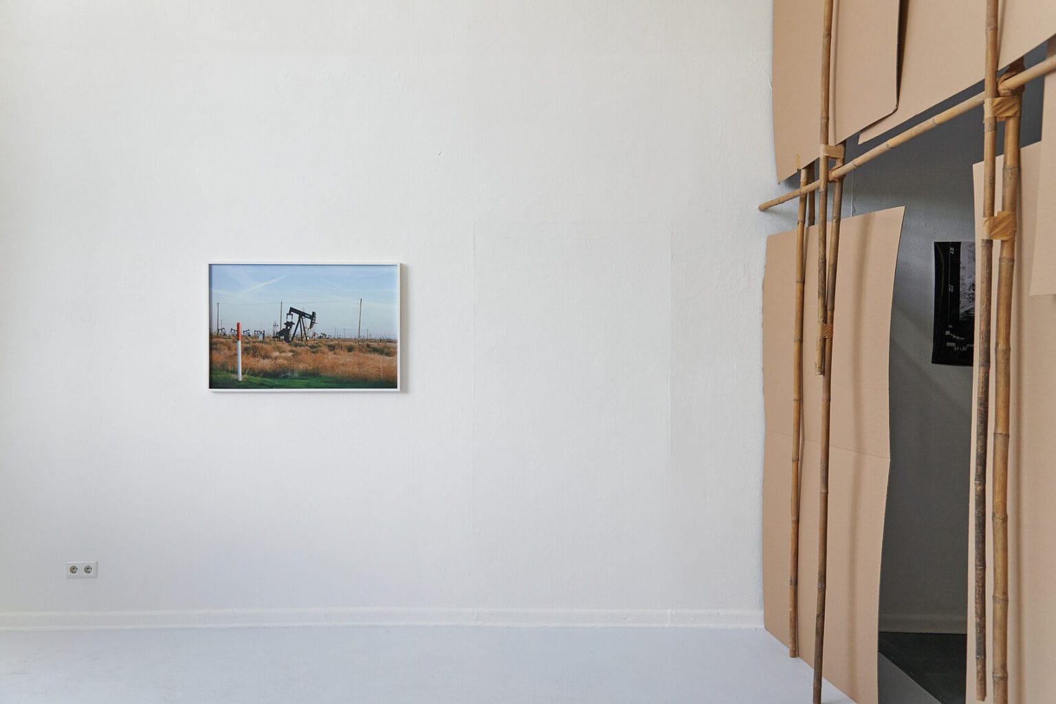 Foto: Ein gerahmtes Objekt hinter Glas an der Wand. Rechts im Raum eine Wand aus ineinander gesteckten Pappen und Hölzern.