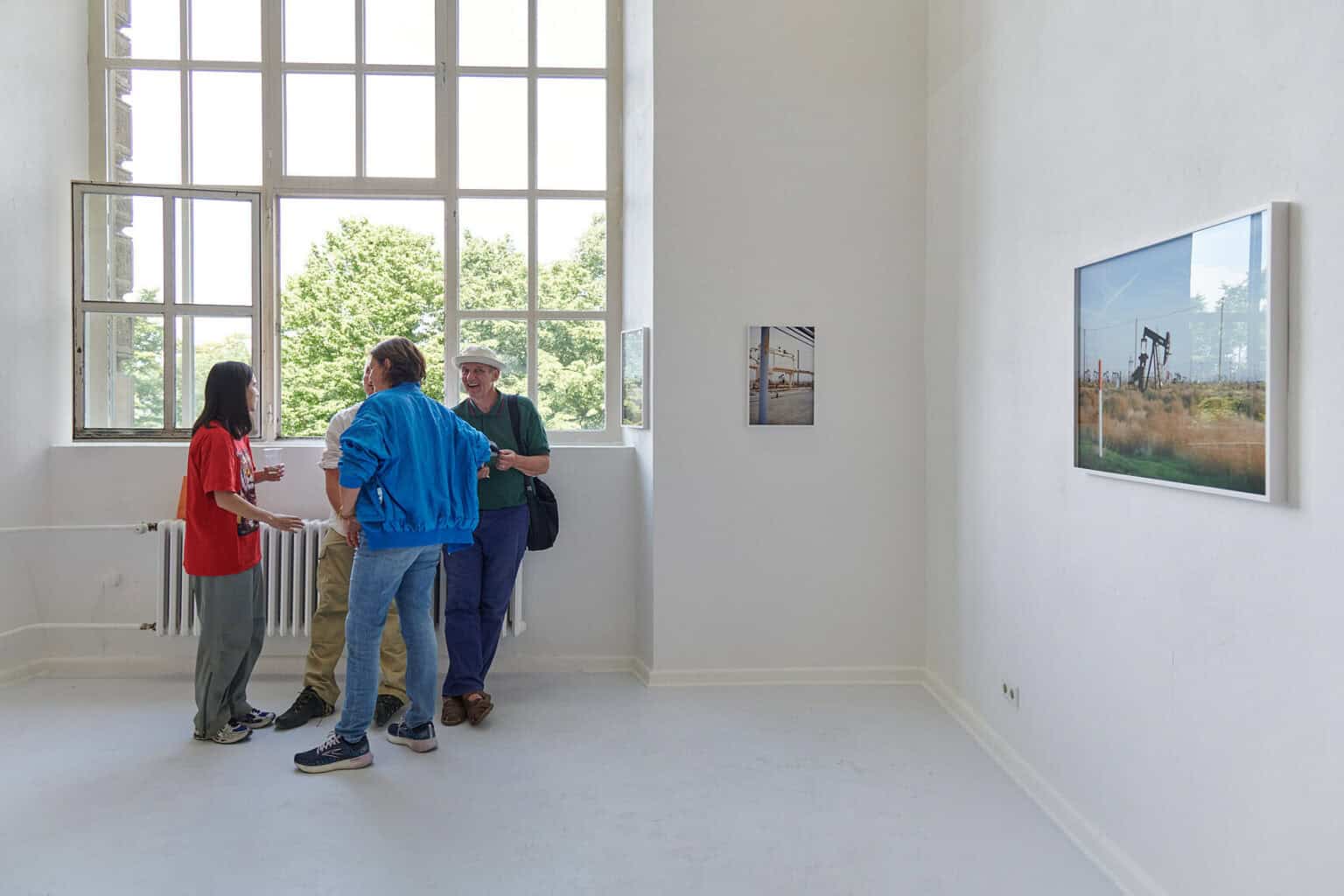 Foto: Ein Raum mit weißen Wänden und hellgrauem Boden. An den Wänden gerahmte Objekte hinter Glas. Im Raum stehen mehrere Menschen.
