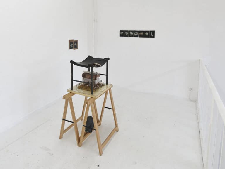 Foto: Ansicht eines Raumes mit weißen Wänden, weißem Boden und weißem Geländer. An den Wänden befinden sich flache Objekte, im Raum steht ein weiteres Objekt.