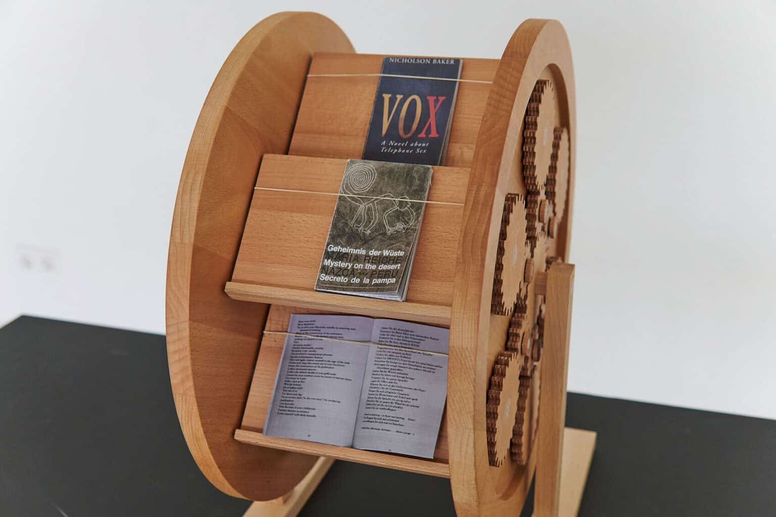 Foto: Ein reifenförmiges Objekt auf schwarzer Oberfläche. In dem Objekt liegen geöffnete und geschlossene Bücher und Hefte.