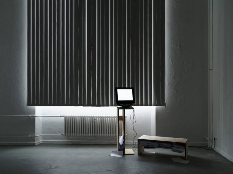 Foto: Ansicht eines mit Lamellen-Gardienen abgedunkelten Raumes. Im Raum befindet sich eine Sitzgelegenheit und eine Konstruktion, auf der ein Bildschirm steht.