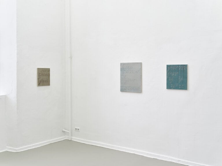 Foto: Ansicht eines Raumes mit weißen Wänden und grauem Boden. An den Wänden hängen, auf gleicher Mittellinie, drei Arbeiten auf Leinwand.