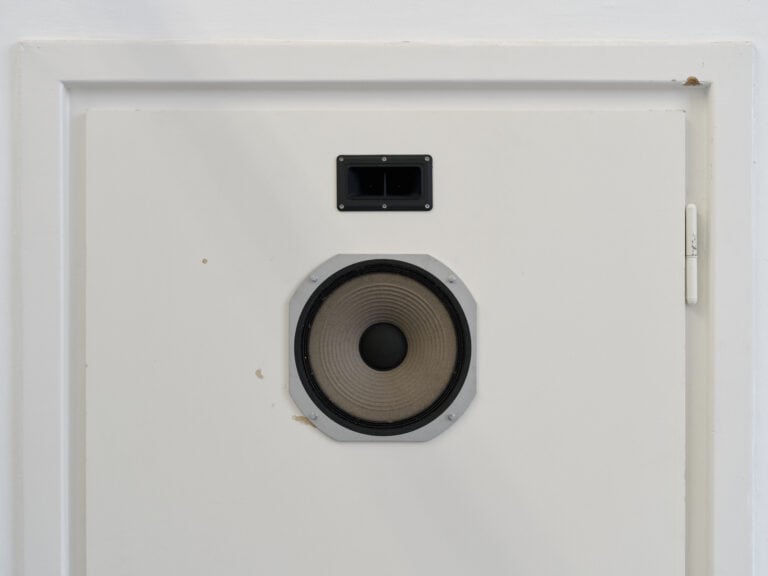 Foto: Nahaufnahme einer mit einem Scharnier versehenen, weißen Platte. In die Platte sind Objekte eingelassen.