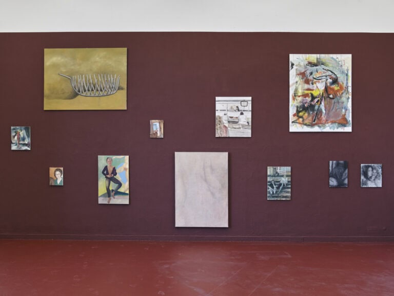 Foto: Ansicht eines Raumes mit einer lila Wand und einem weinroten Boden. An den Wänden hängen in unterschiedlichen Höhen Malereien in Klein-, Mittel- und Großformaten.