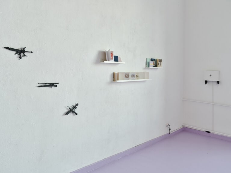 Foto: Aufnahme einer Raumecke mit weißen Wänden und violettem Boden. An den Wänden befinden sich auf unterschiedlichen Höhen Objekte.