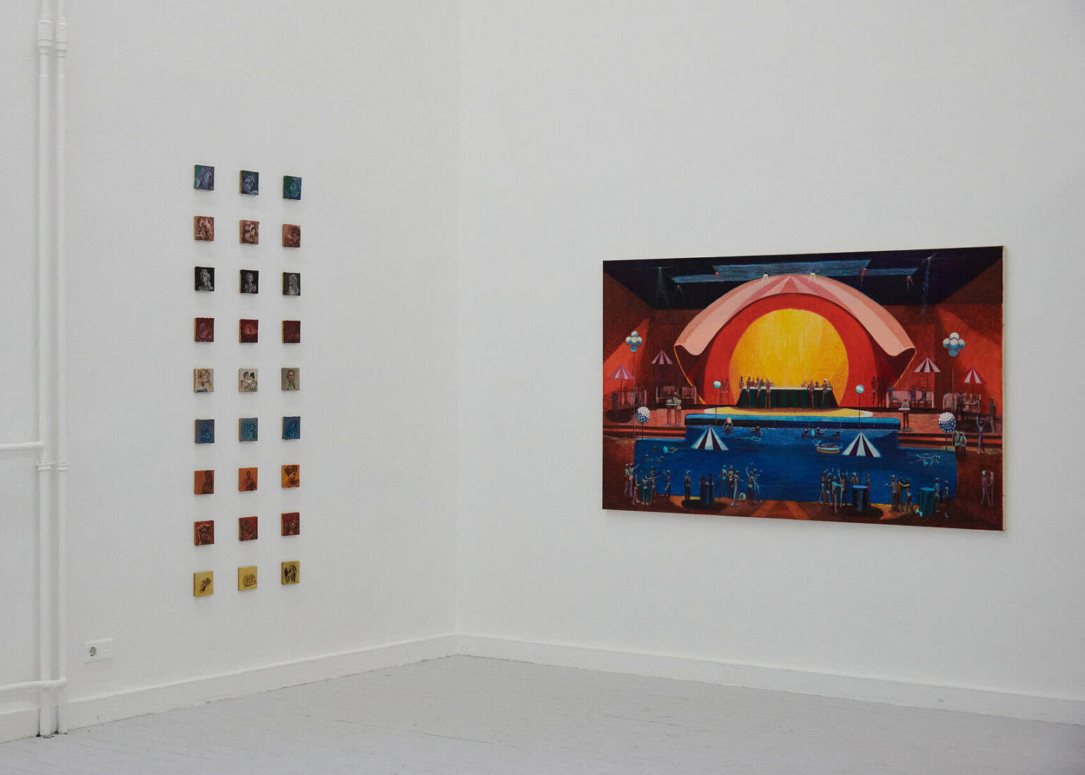 Foto: Ansicht eines Raume mit weißen Wänden und grauem Dielenboden. An den Wänden hängt eine Gruppe aus kleinformatigen, quadratischen Objekten, die im gleichen Abstand zueinander in mehreren Reihen hängen und eine großformatige Arbeit auf Leinwand.