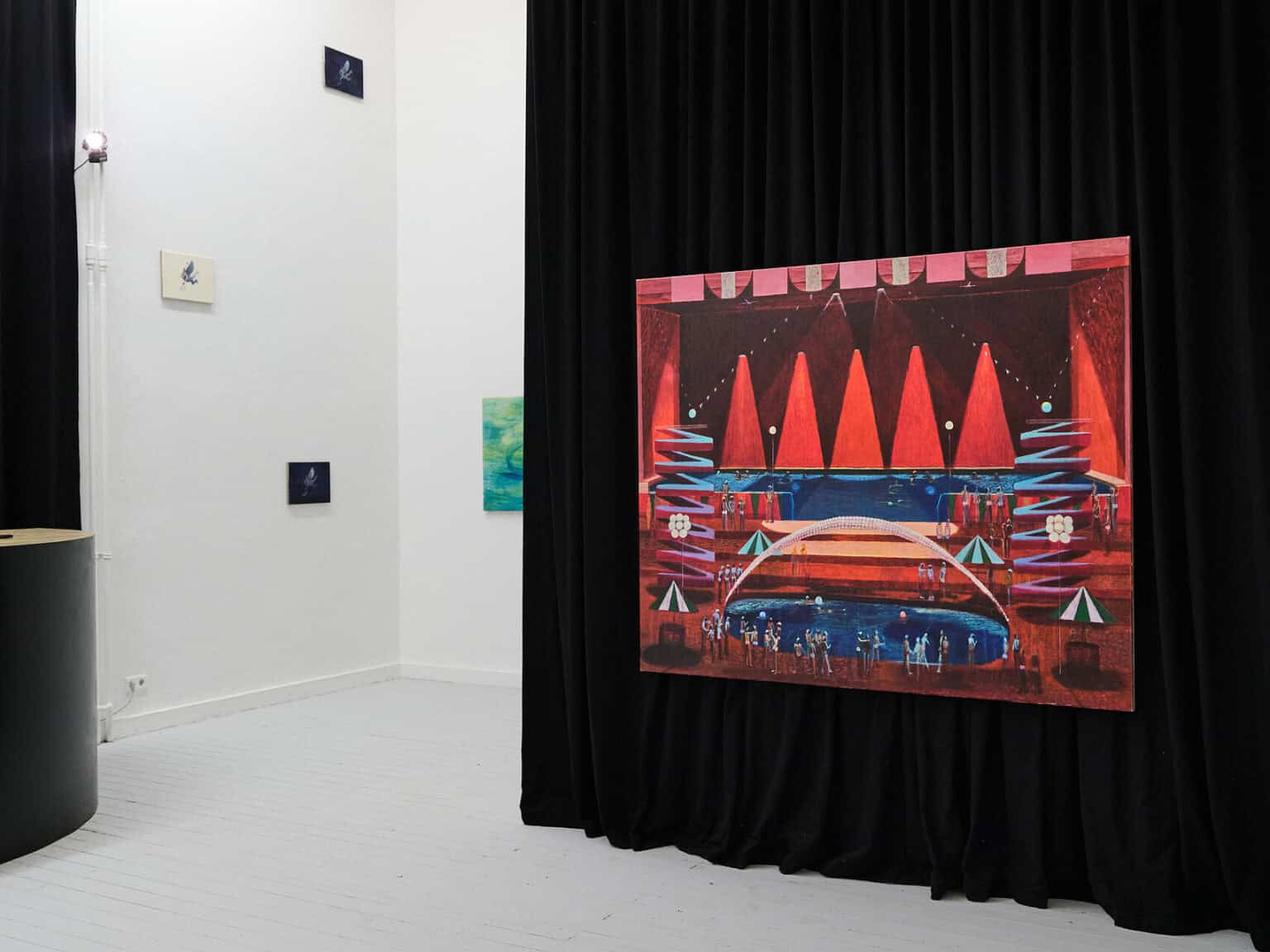 Foto: Ansicht eines Raumes mit weißen Wänden und hellgrauem Dielenboden. An den Wänden befinden sich, auf unterschiedlicher Höhe, kleinformatige Leinwandarbeiten. Im Raum hängt ein dunkler Vorhang, vor dem eine großformatige Leinwand installiert ist.