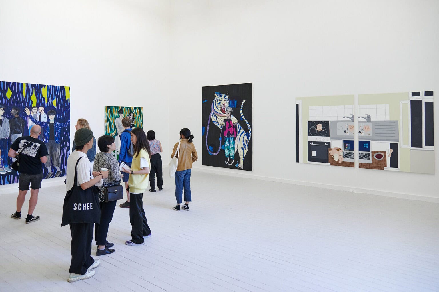 Foto: Ein Raum mit weißen Wänden und grauem Dielenboden. An den Wänden hängen viele große Leinwände. Im Raum stehen und bewegen sich einige Menschen.