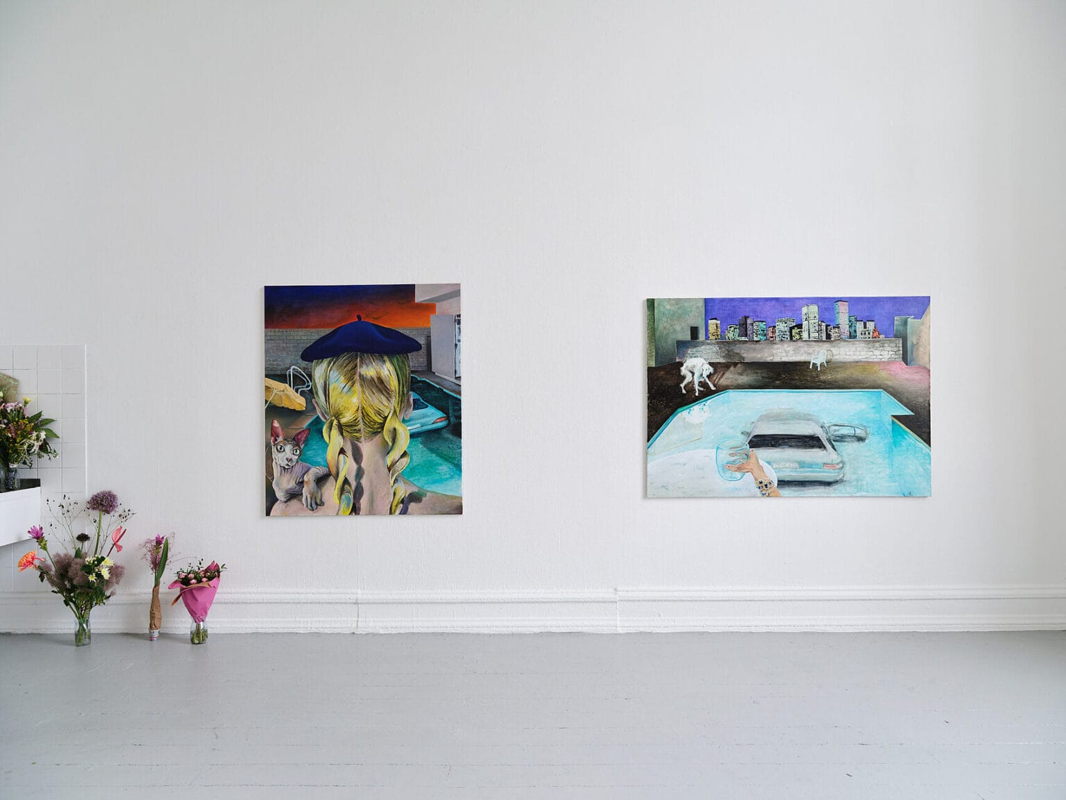 Foto: Ansicht eines Raumes mit weißen Wänden und grauem Boden. An der Wand hängen zwei Leinwandarbeiten im Mittelformat. Links im Bild stehen Blumensträuße auf dem Boden.