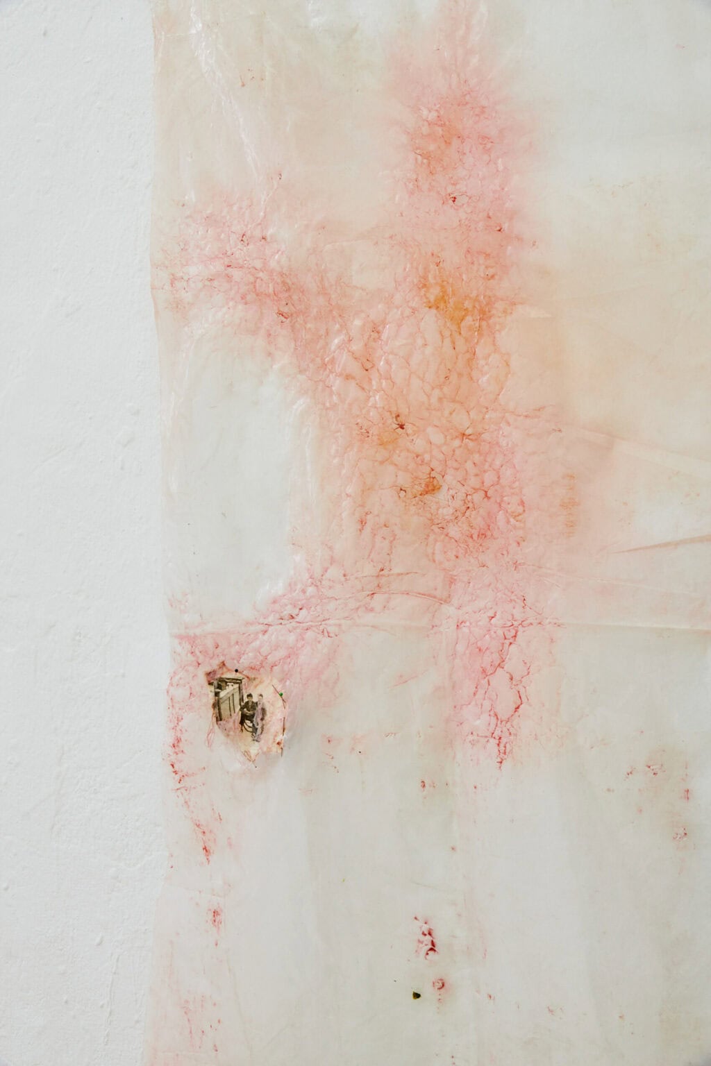 Foto: Nahaufnahme eines Objektes aus hellem Material mit unebener, rissiger und in manchen Teilen eingefärbter Oberfläche. Auf das Objekt ist eine Fotografie montiert.