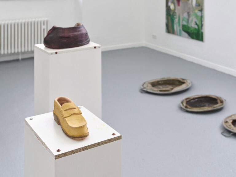 Foto: Ansicht eines Raumes mit weißen Wänden und grauem Boden. An der Wand hängt eine Malerei. Auf dem Boden des Raumes und auf Sockeln befinden sich Objekte.