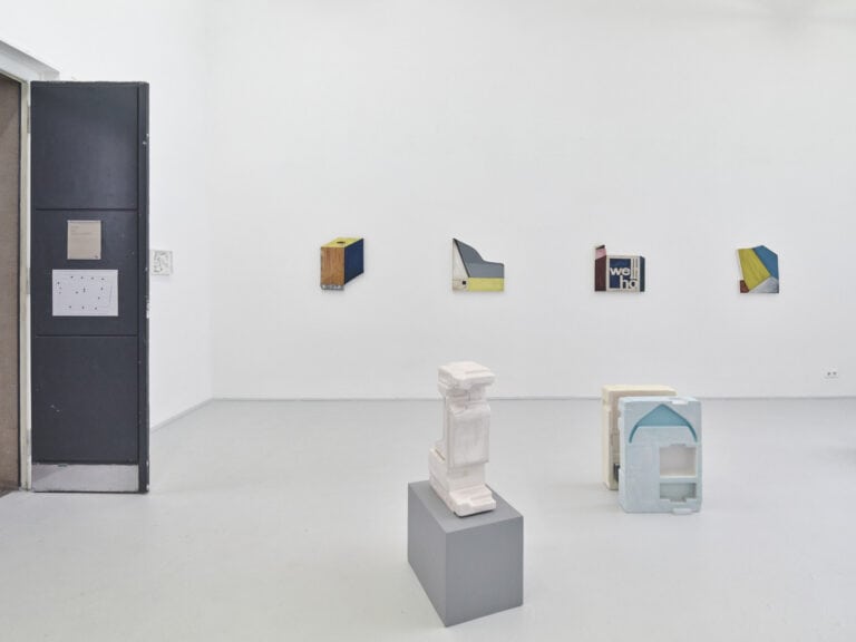 Foto: Ansicht eines Raumes mit weißen Wänden und grauem Boden. An den Wänden befinden sich Objekte im Klein- und Mittelformat. Im Raum befinden sich weitere Objekte, die zum Teil auf Sockeln stehen.