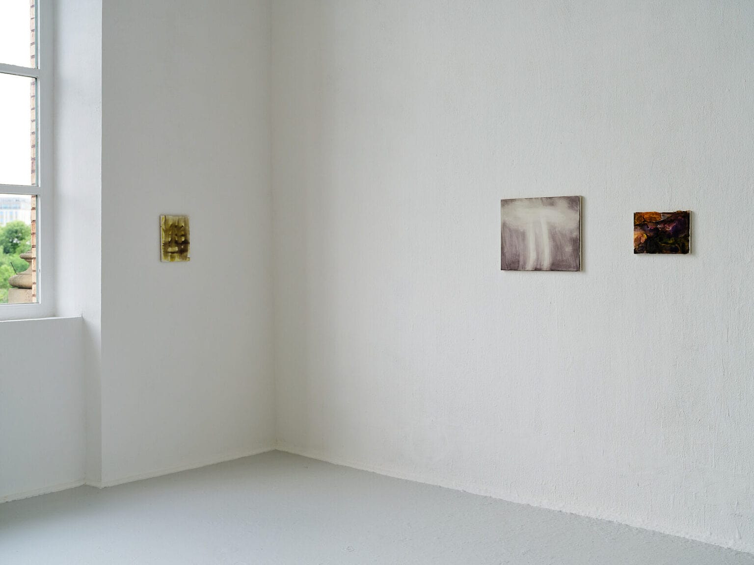 Foto: Ansicht eines Raume mit weißen Wänden und grauem Boden. An den Wänden hängen, auf gleicher Mittellinie, kleinformatige Leinwandarbeiten.