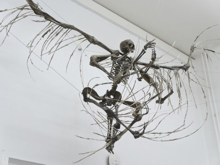 Foto: Nahaufnahme eines Objektes vor einer weiße Wand. Das Objekt ist an Seilen befestigt.