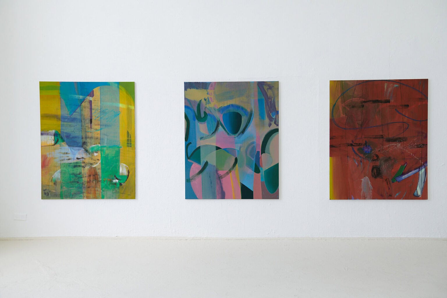 Foto: Ein Raum mit weißer Wand und beigem Boden. An der Wand hängen drei großformatige Leinwände im gleichen Format und im gleichen Abstand zueinander.