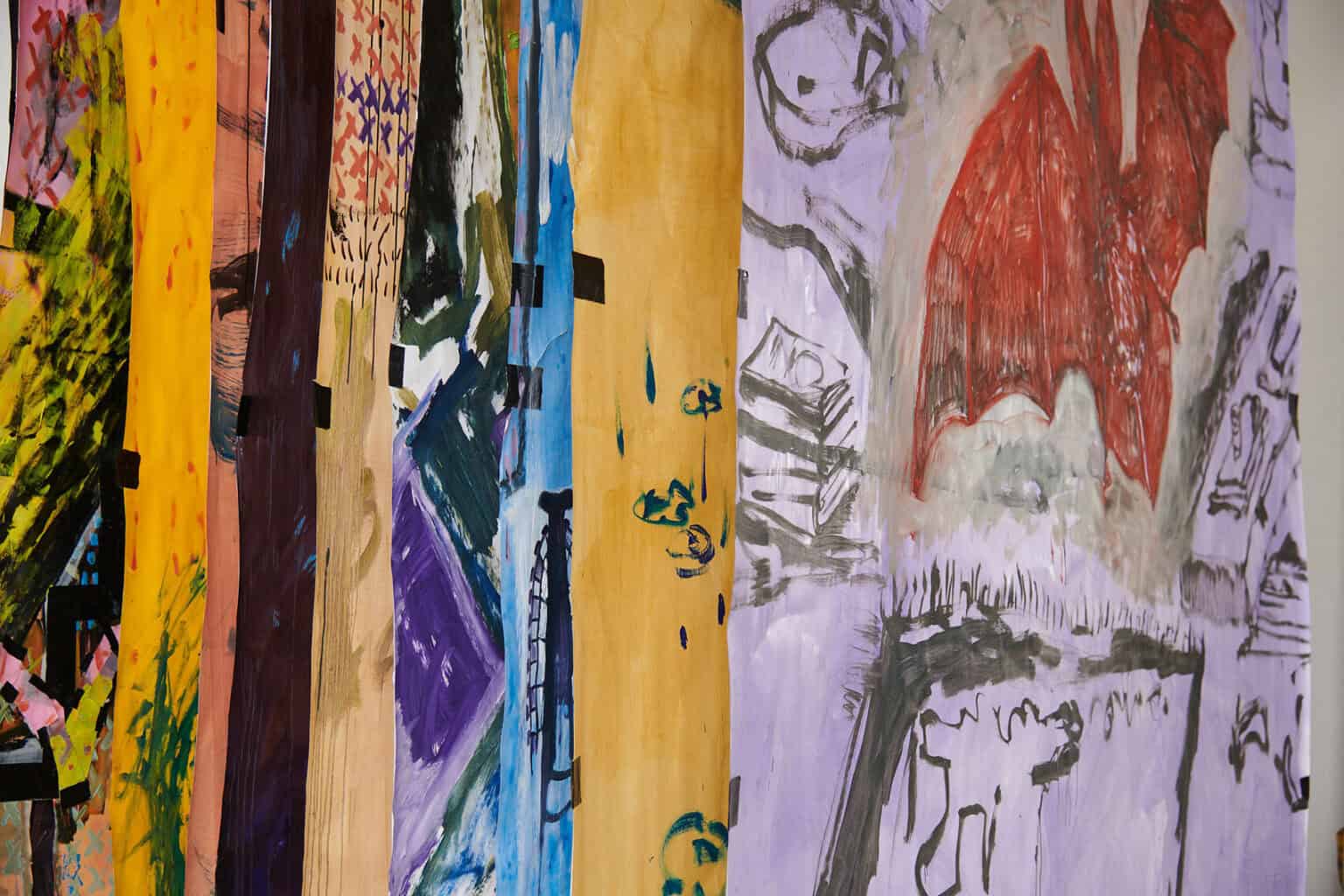 Foto: Detailaufnahme mehrerer mit Farbe bearbeiteter Papier, die hintereinander hängen.