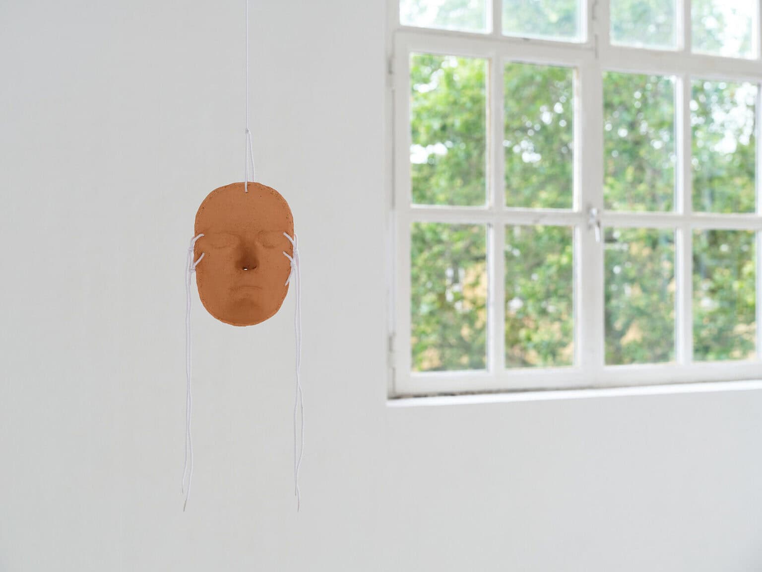 Foto: Ansicht eines von der Decke hängenden Objektes in einem Raum mit weißen Wänden und Fenster.