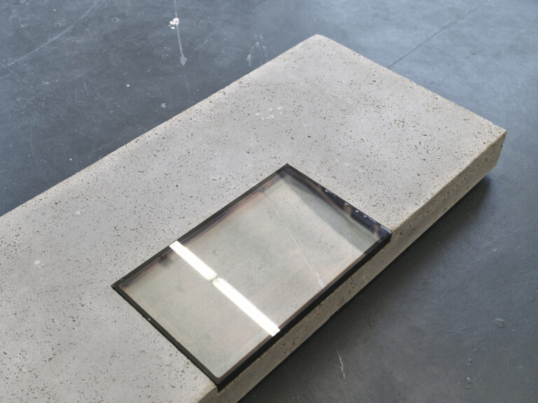 Foto: Nahaufnahme eines Objekts, dass auf dunklem Boden liegt. In der reflektierenden Oberfläche spiegelt sich das Deckenlicht.