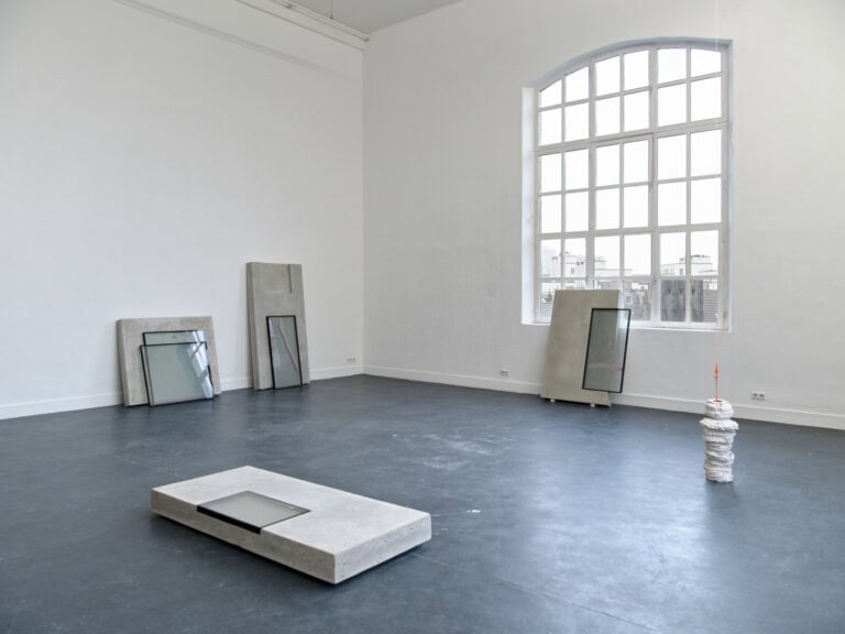 Foto: Ansicht eines Raumes mit weißen Wänden, dunklem Boden und einem Bogenfenster. Im Raum stehend und liegend befinden sich Skulpturen. Weitere von Ihnen sind an die Wände gelehnt.