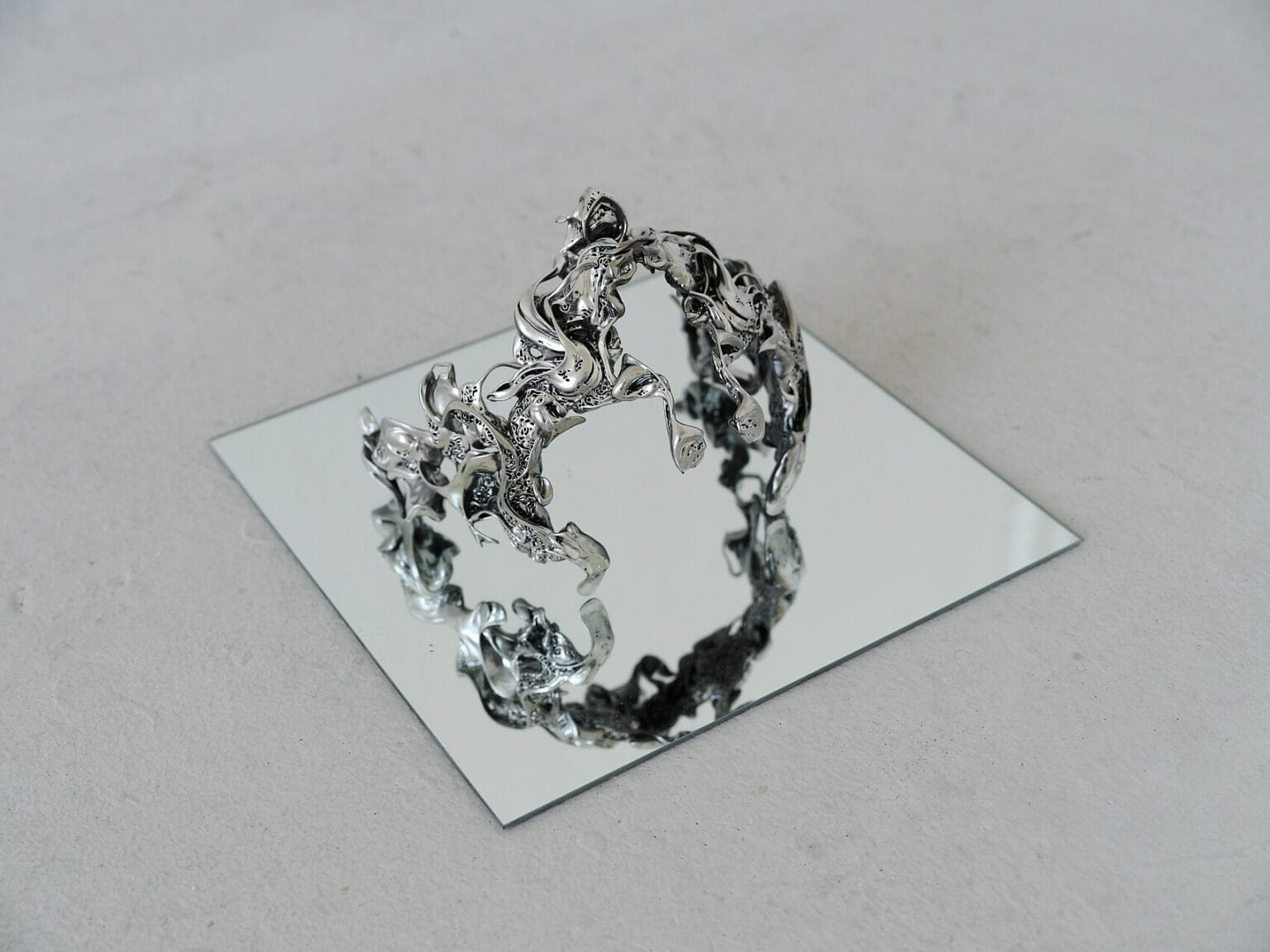 Foto: Nahaufnahme eines Objektes auf spiegelnder Oberfläche auf einem grauem Boden.