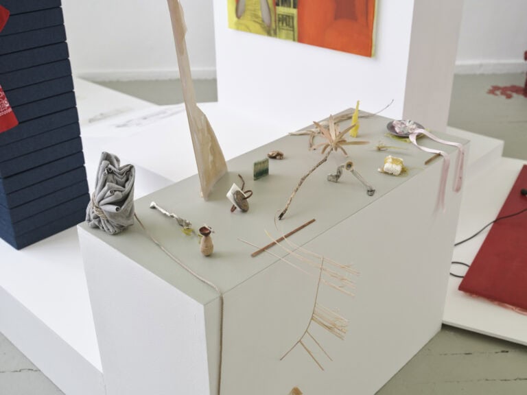 Foto: Nahaufnahme einer verschachtelte Plattform, auf der Objekte aus unterschiedlichen Materialien liegen. Die Plattform steht auf einem gtünlich- grauen Dielenboden.