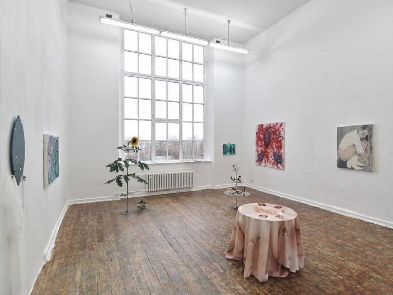 Foto: Ansicht eines Raumes mit weißen Wänden, braunem Dielenboden und einem großen Fenster. An den Wänden hängen Malereien und Objekte. Im Raum befinden sich weitere Skulpturen.