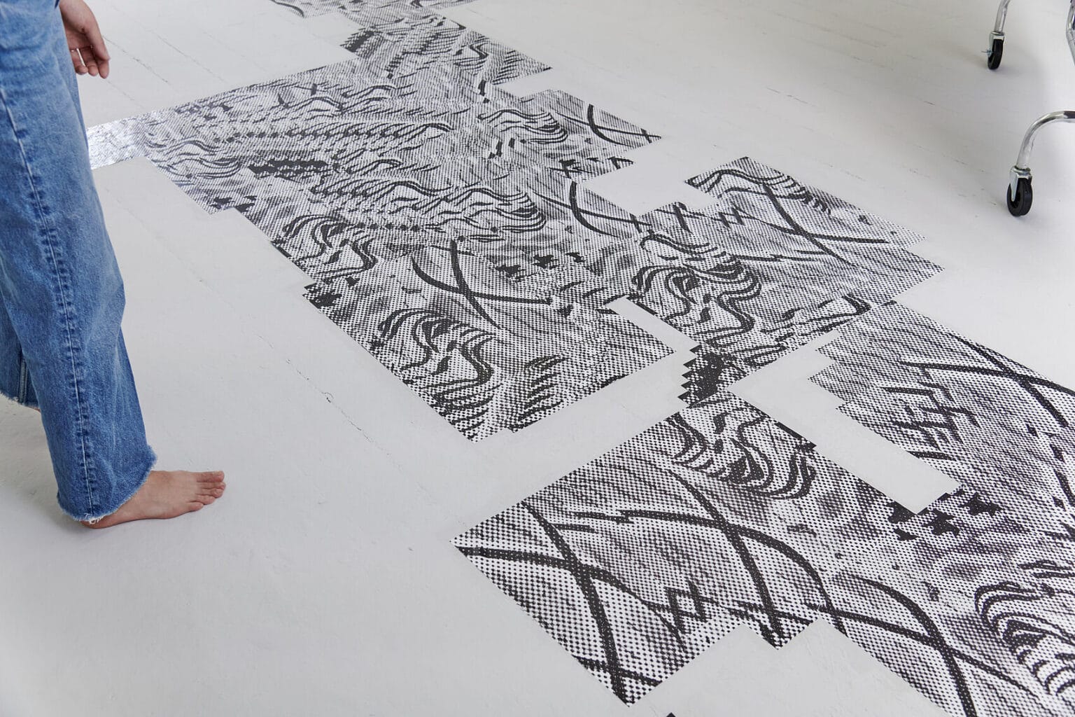 Foto: Eine Gruppe von flachen, gemusterten Objekten, die sich über den Boden erstreckt. Links im Bild eine barfüßige Person.