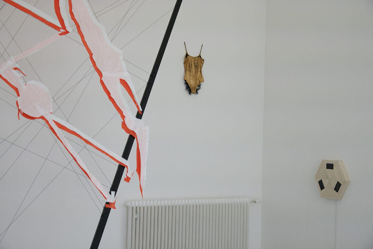 Foto: Ein Raum mit weißen Wänden, an denen auf unterschiedlicher Höhe Objekte hängen. Im Raum eine Skulptur.