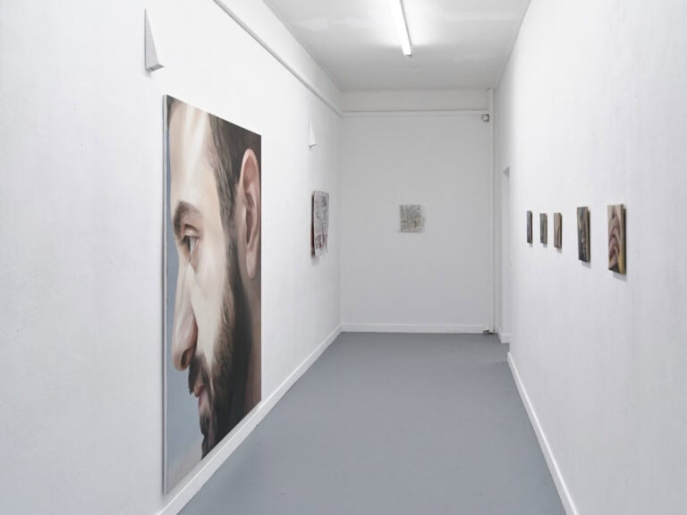 Foto: Ansicht eines länglicher Raumes mit weißen Wänden und grauem Boden. An den Wänden befinden sich Malereien in Klein- Mittel- und Großformaten.