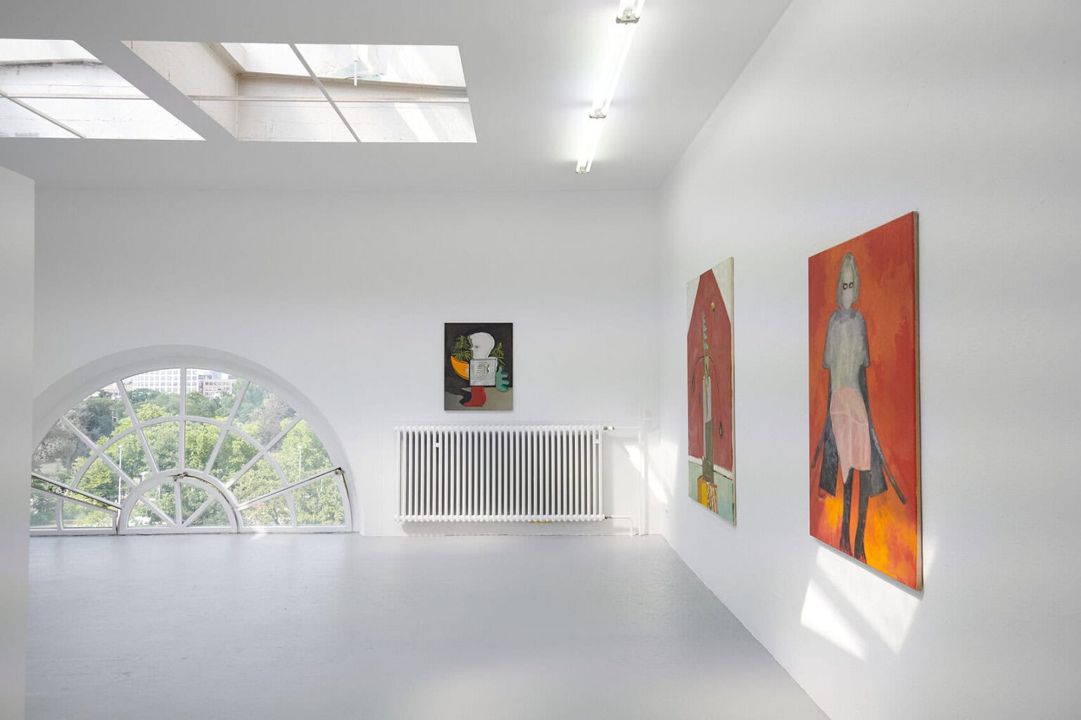 Foto: Ein Raum mit weißen Wänden, grauem Boden und kleinem Bogenfenster. An der Wand hängen Leinwände im Mittel- und Großformat.