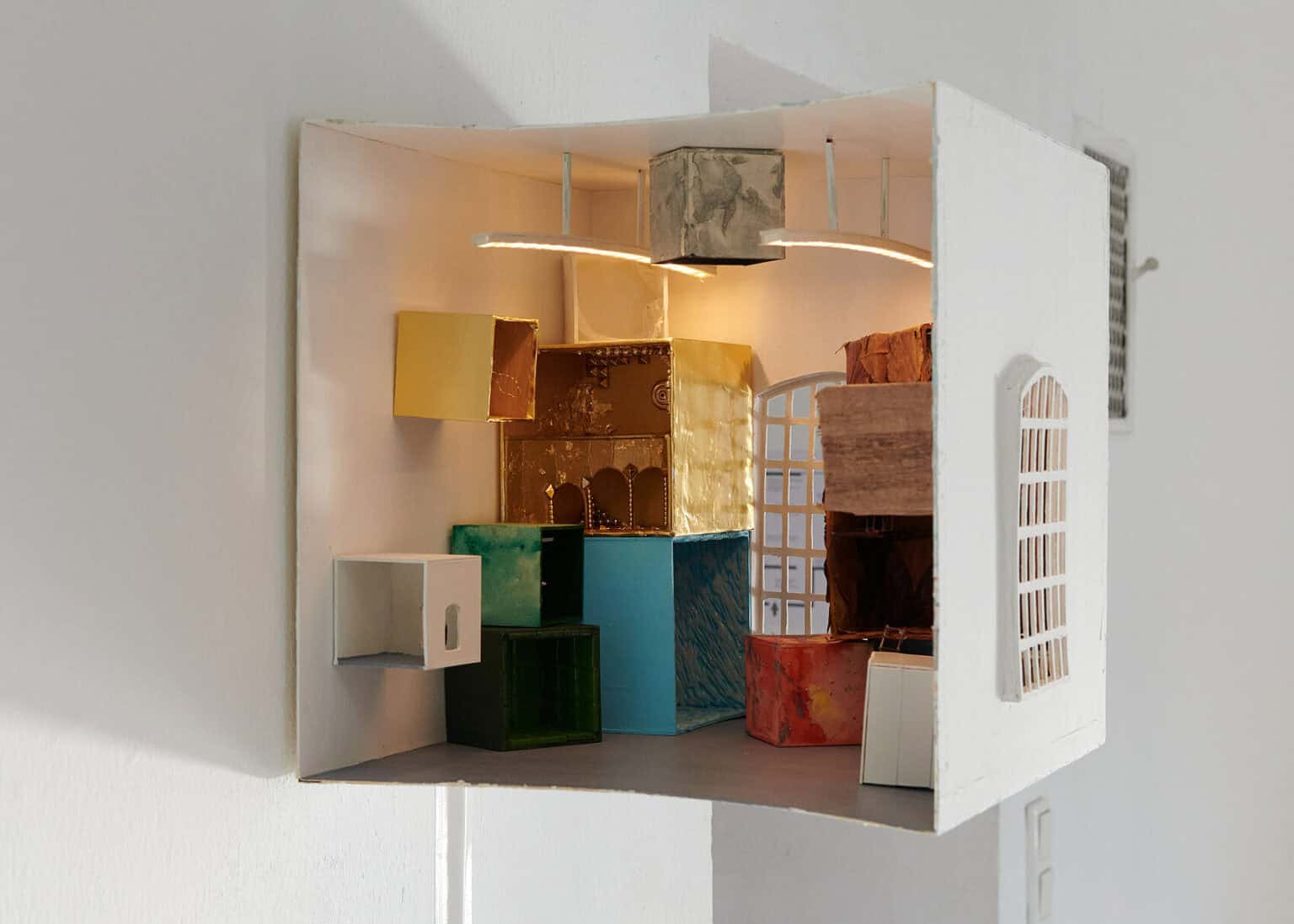 Foto: Nahaufnahme eines kastenförmigen Objektes, in dem sich weitere rechteckige und leuchtende Objekte befinden, vor einer weißen Wand.