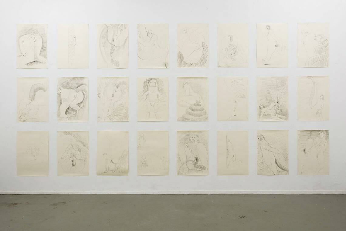 Ein Raum mit weißen Wänden und grauem Boden. An der Wand eine Vielzahl von Papierarbeiten im gleichen Format, die in drei Reihen untereinander im immerzu gleichen Abstand neben- und untereinander hängen.