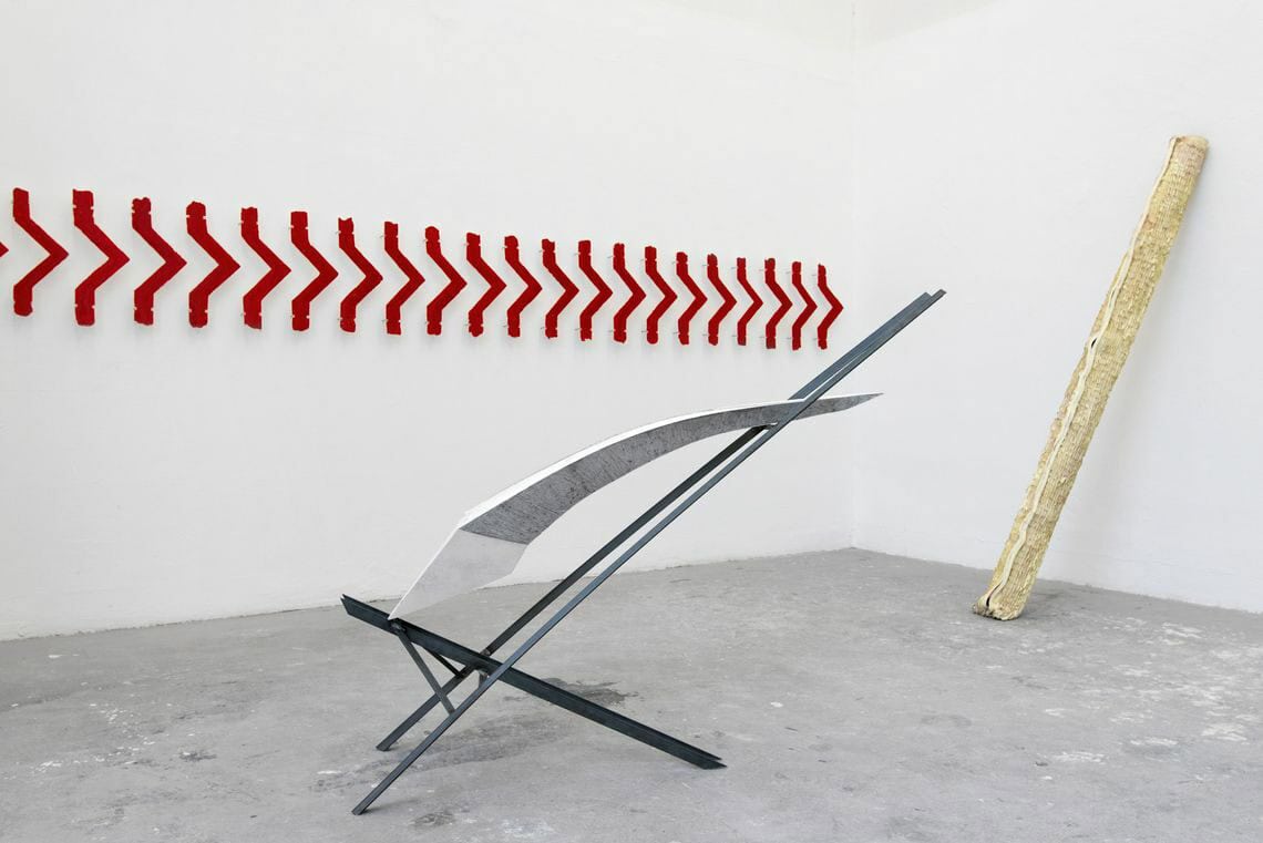 Foto: Ein Raum mit weißen Wänden und grauem Boden. Im Raum und an der Wand befinden sich mehrere Objekte aus unterschiedlichen Materialien.