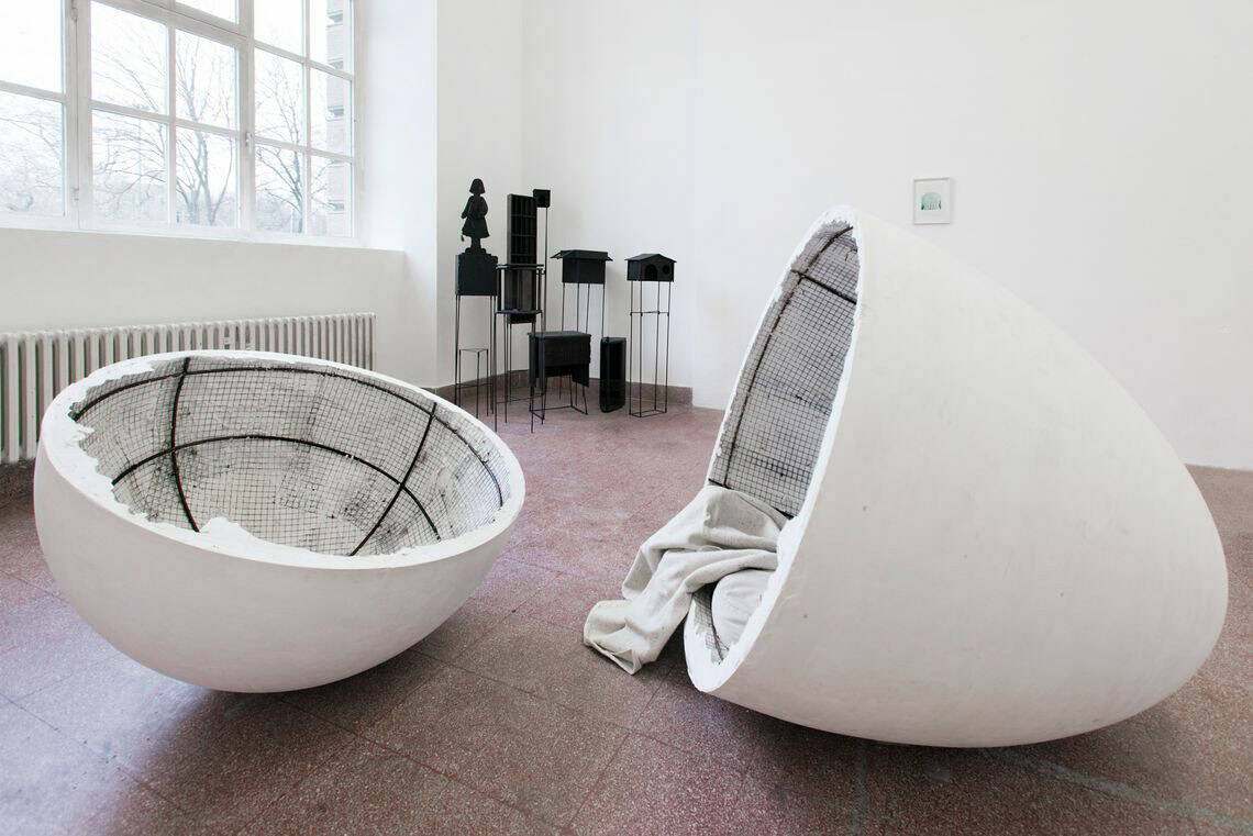 Foto: Ein Raum mit weißen Wänden, rotem Steinboden und einem großen Fenster. Im Raum stehen mehrere Gruppen von Skulpturen. Manche von ihnen sind sehr groß. An der Wand hängt ein kleine gerahmtes Objekt.