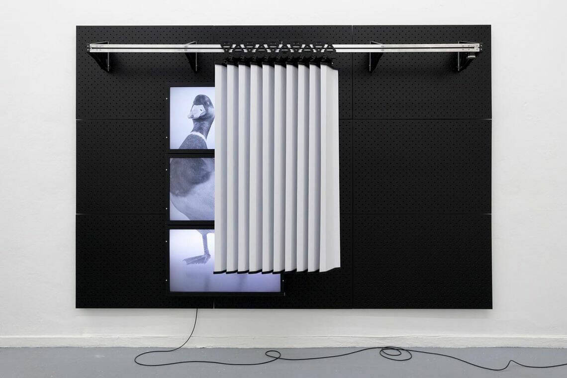 Foto: Ein großformatiges Objekt vor einer weißen Wand. Es besteht auf unterschiedlichen Materiellen und ist an ein Kabel angeschlossen.