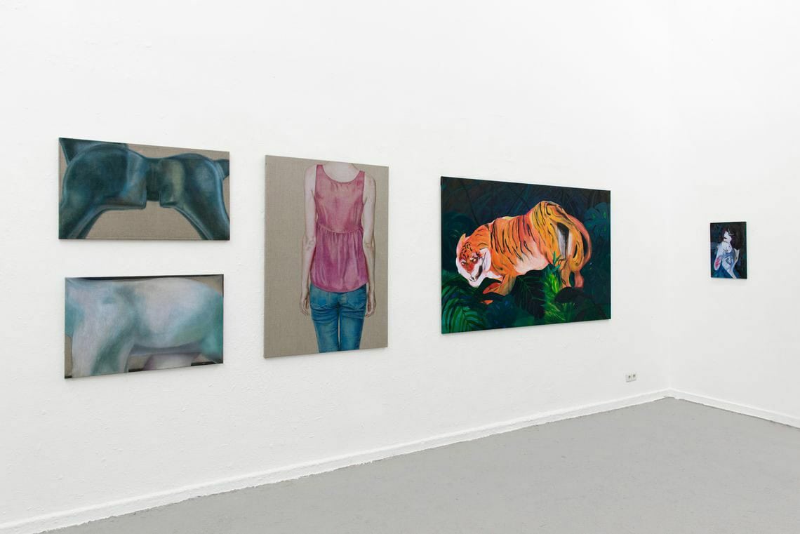 Foto: Ein Raum mit weißen Wänden und grauem Dielenboden. An der Wand hängen mehrere Leinwände im Klein- und Mittelformat in einem Streifen.