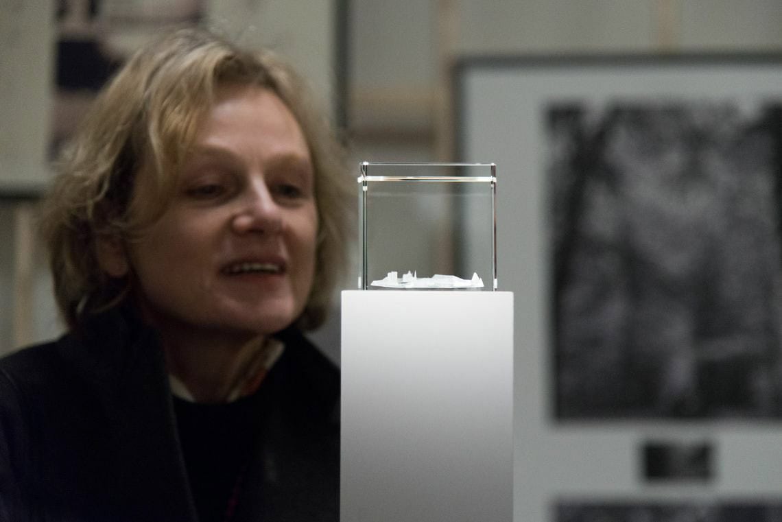 Foto: Ein Kleines Objekt auf einem kleinen Sockel. Dahinter der Oberkörper und das Gesicht eines Menschen.